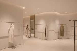 A minimalist fashion store with white walls and clothing racks.