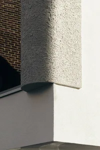 White concrete exterior wall with textured finish and shadow details.