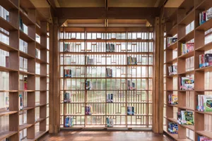 A spacious library interior featuring tall wooden shelves filled with books and a central glass wall