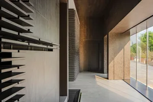 Modern, minimalist corridor with concrete walls, slatted feature wall, and large windows overlooking greenery.
