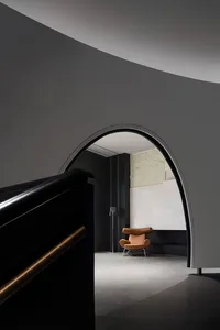 A minimalist interior design featuring dark concrete walls with an arched doorway leading to a lounge area with a single mode