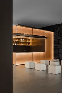Modern bar counter featuring metallic texture, illuminated with warm lighting, and accompanied by minimalist seating.