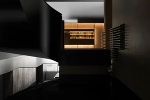 A modern bar area featuring wooden panels with dim lighting and bottles displayed on shelves.