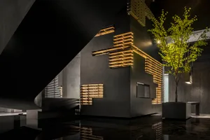 A modern hotel lobby featuring dark metallic cladding and illuminated wood slats.
