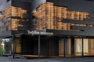 A modern storefront featuring a metal facade with a geometric design and illuminated signs.