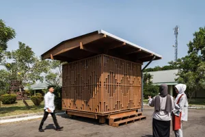 A wooden urban structure with a geometric design, featuring a flat roof and a grid of vertical wooden elements.