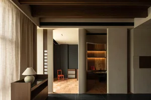 Modern home office with concrete walls and floor tiles, featuring wooden furniture and a red chair.