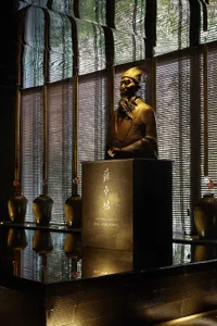 Bronze statue of a man with long beard, wearing a traditional hat and robe, placed on a pedestal.