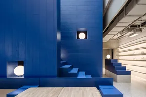Industrial-style interior design featuring blue walls and stairs with a wooden table and white lamps.