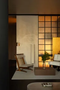 A minimalist living room featuring a glass window with a textured surface, a wooden chair, a wooden coffee table, and a white