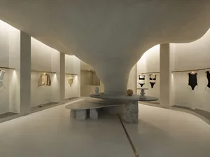 A minimalist retail store with concrete walls and stone tables, featuring clothing on racks.