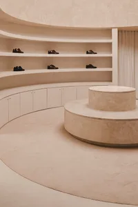 A minimalist retail space featuring concrete shelving and neatly arranged black leather shoes.