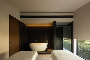 Minimalist spa room with a freestanding bathtub, massage beds, and glass walls