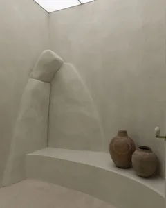Minimalist bathroom featuring textured concrete wall and floor, with two decorative pots.