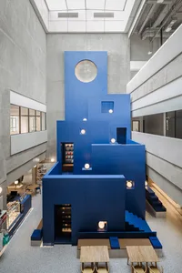 A modern indoor space with blue structures, white lighting, and wooden tables.
