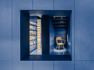 A minimalist library interior with blue walls, wooden shelves, and a wooden chair.