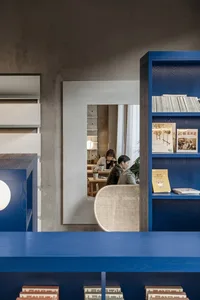 A modern library interior featuring blue wooden shelves with books and a woven chair.