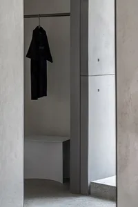 A minimalist wardrobe space featuring concrete elements and a single black garment hanging on a rod.