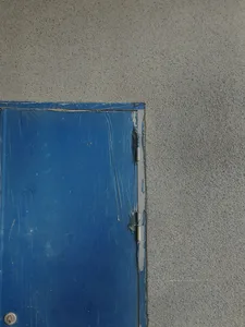 一道磨損的藍漆門，安裝在質感豐富的灰色混凝土牆面上。