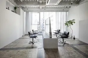 A minimalist modern hair salon with white walls, black chairs, and a concrete floor.