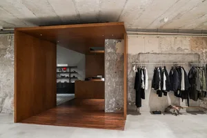 An industrial-style clothing retail space featuring a wooden podium and concrete walls.