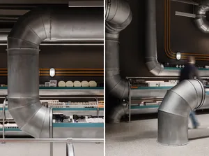 A retail storefront featuring large, metallic pipes against a dark, textured wall, creating an industrial aesthetic.