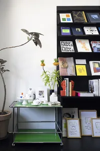 A modern bookshelf display featuring a variety of books, plants, and decorative items on a green rolling cart in an indoor se