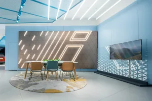 A modern conference room with a geometric backdrop, wooden chairs, a round rug, and a television displaying a landscape image