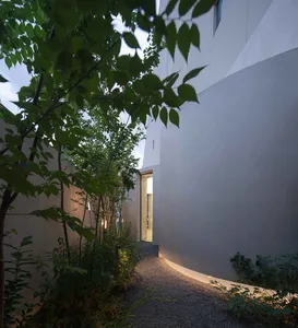 A serene, minimalist pathway enclosed by smooth concrete walls and adorned with lush greenery and soft lighting.
