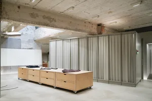 Modern interior space featuring concrete walls, wooden cabinets, and clothing displayed on a table.