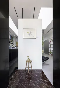 A minimalist entryway with a unique shaped stool and a plant on top, featuring dark marble flooring.