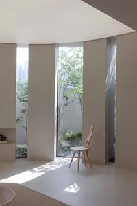 Modern, minimalist living room with concrete walls, large glass windows, and a single wooden chair