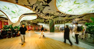 A modern shopping center interior with a metal accent wall decorated with green plants and a tree