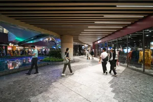 People walking in a modern shopping mall featuring concrete, glass, and tile flooring.