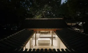 A traditional Japanese teahouse with black tiled roofs and white walls illuminated by lights at dusk.
