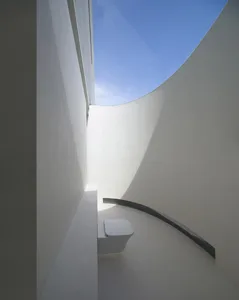 A minimalist bathroom with white concrete walls and a skylight.
