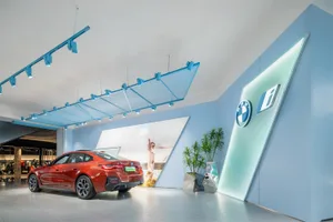 A modern car dealership showroom with a red car on display, blue lighting, and green plants.