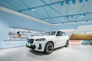 A white BMW SUV with blue accents displayed in a modern showroom with blue ceiling panels.