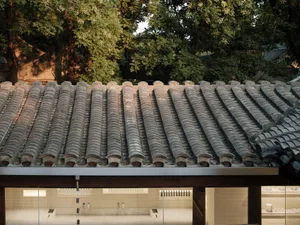 A traditional roof with curved tiles against a backdrop of lush green trees.