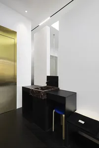 A minimalist bathroom featuring metal and marble elements, with a sleek black vanity and white walls.