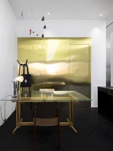 A minimalist office with a transparent glass desk, wooden chair, and metallic accents.