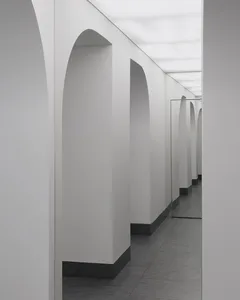 A minimalist corridor with white walls, grey concrete flooring, and arched doorways.