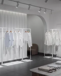 A minimalist fashion shop featuring white clothes on metallic frames and a clean, modern aesthetic