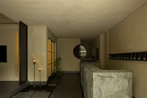 A minimalist lobby featuring stone walls and floor, with a circular window and a shelf with small dishes.