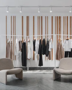 A minimalist clothing store interior with white racks, metallic rails, and wooden backdrop.