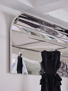 A black garment hangs from a metallic hanger on a mirrored surface in a minimalist clothing showroom.
