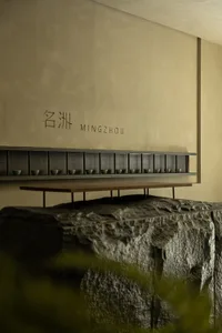 極簡酒吧，木質座椅搭配石材牆面，牆上掛架擺放小杯。