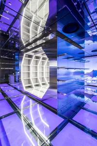 Modern minimalist exhibition space featuring glass walls, metallic structures, and ambient lighting.