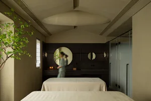 A minimalist spa room featuring dark wood, with a person walking behind a desk with candles.