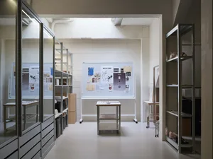 A minimalist workspace featuring metal shelving units and a whiteboard with various papers pinned to it.